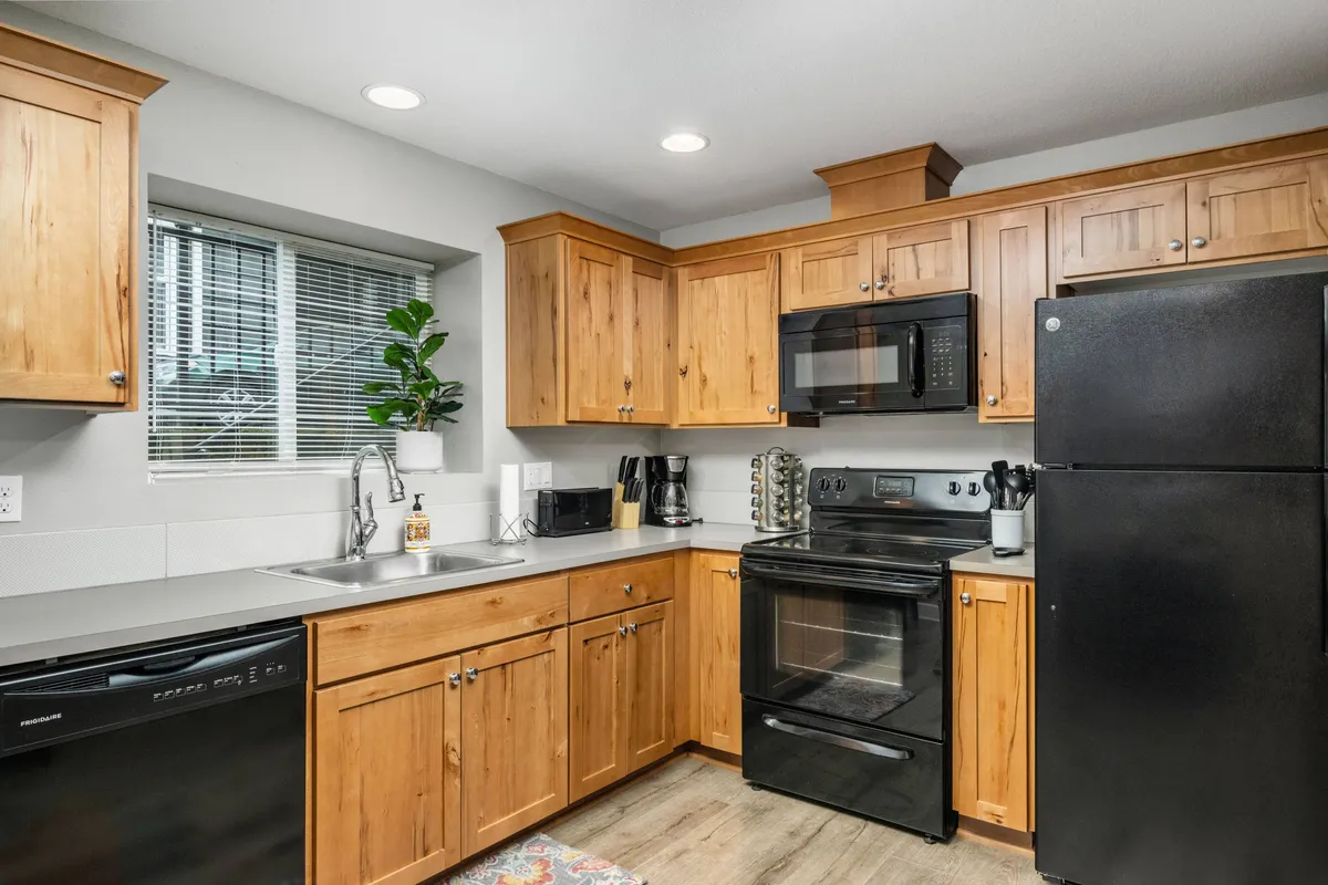 This image captures a warm, inviting kitchen space featuring wooden cabinetry, sleek black appliances, and a window looking out onto leafy greenery. The scene feels bright and tucked away, with natural daylight enhancing the cozy, tranquil atmosphere—a perfect setting for unwinding after a day of city exploration.