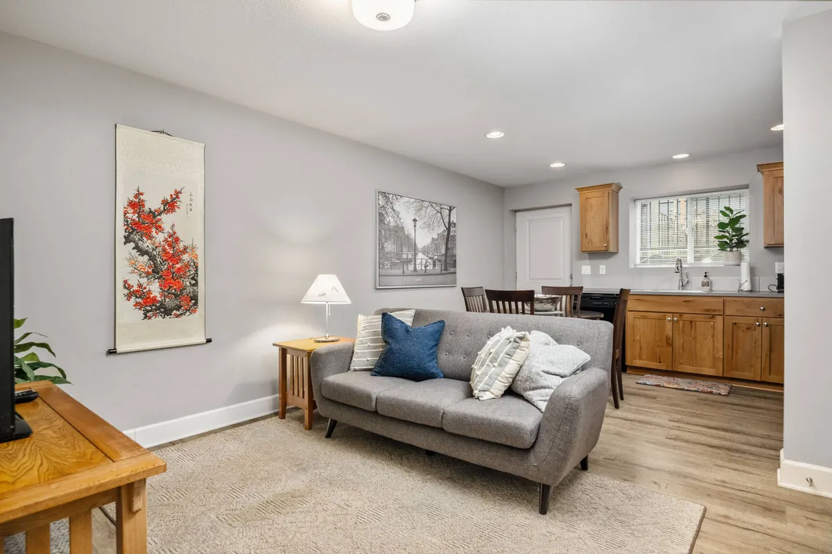 A welcoming living area featuring a sofa with decorative pillows, a TV stand, and a dining area with a wooden table and chairs. Wall art and soft lighting create a cozy, inviting vibe, perfect for relaxing, enjoying meals, or socializing.