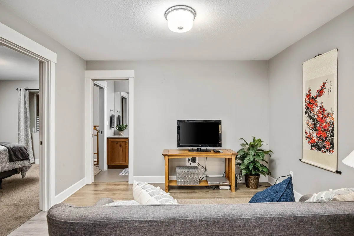 A cozy living room area featuring a full-size sofa bed, a television, vibrant green plants, and colorful artwork on the walls. The space is bright and inviting, perfect for family relaxation or movie nights after a day of exploring local attractions.