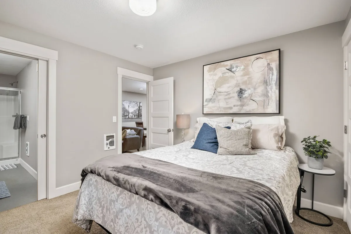 A calm, inviting bedroom space with a comfortable bed, soft lighting from a side table lamp, and art on the wall. The scene emphasizes relaxation and quiet, ideal for peaceful moments or restful sleep.
