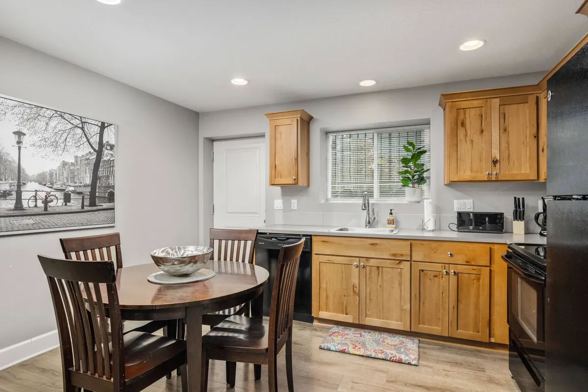 A bright interior view of a dining table set near the kitchen cabinetry, accented by wall art and thoughtful decor. The arrangement encourages family meals, social gatherings, and creative work sessions in a warm, welcoming setting.