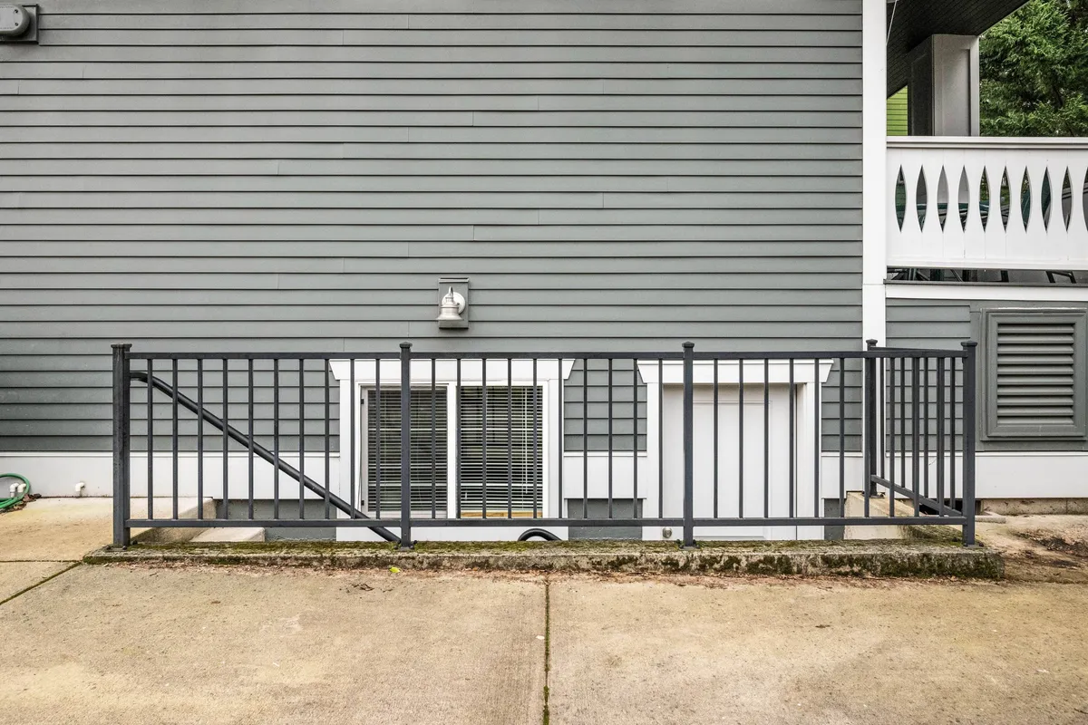 This image captures a metal railing leading down alongside the grey siding of the building, hinting at a lower-level, private entry. The view emphasizes the separation from the main house, with a practical and subtle atmosphere that signals privacy and peace, key to the narrative of retreat.