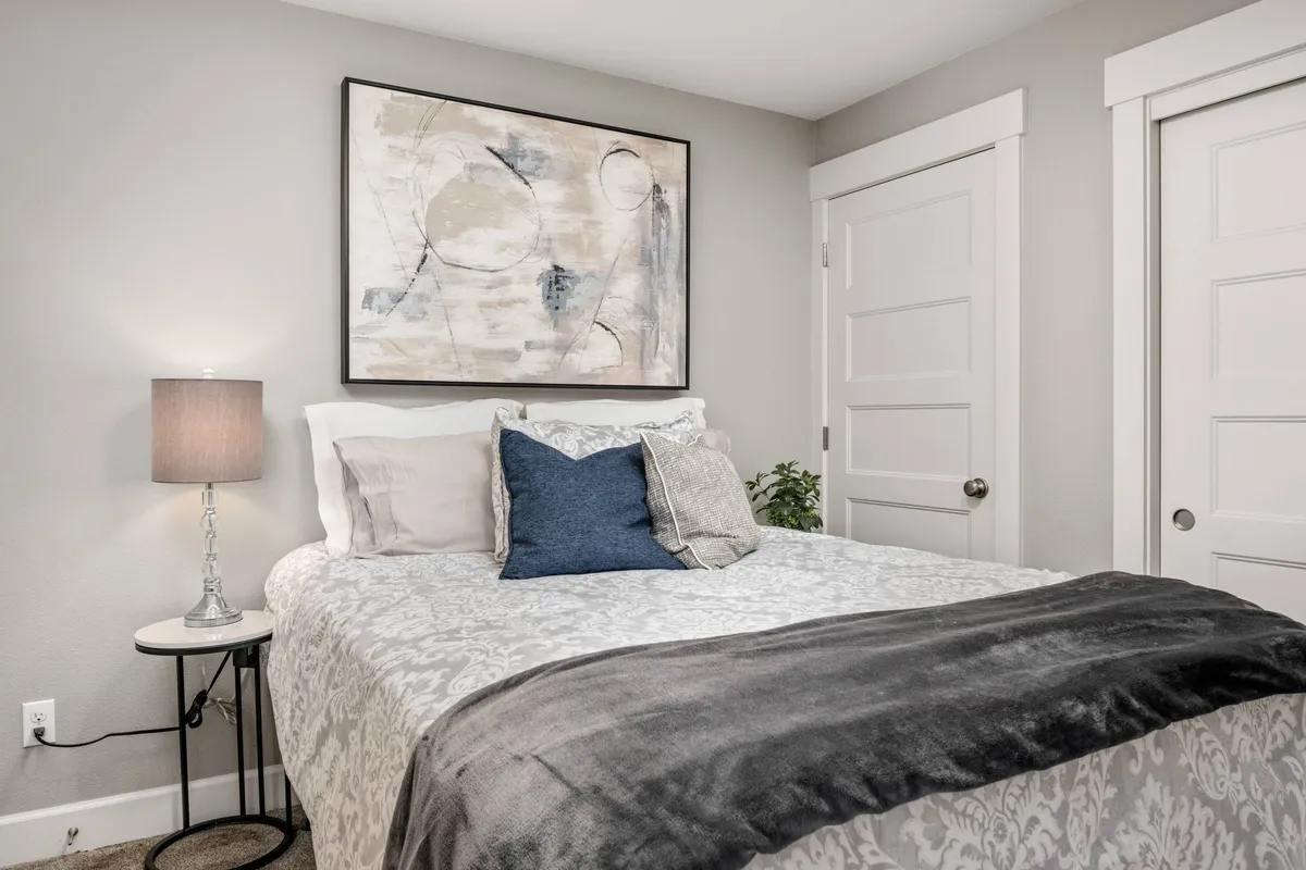A serene bedroom scene featuring a neatly made queen bed with soft linens, a nightstand and lamp, and tasteful artwork on the wall. The gentle lighting and uncluttered decor evoke a tranquil, restful atmosphere perfect for unwinding after a busy day.