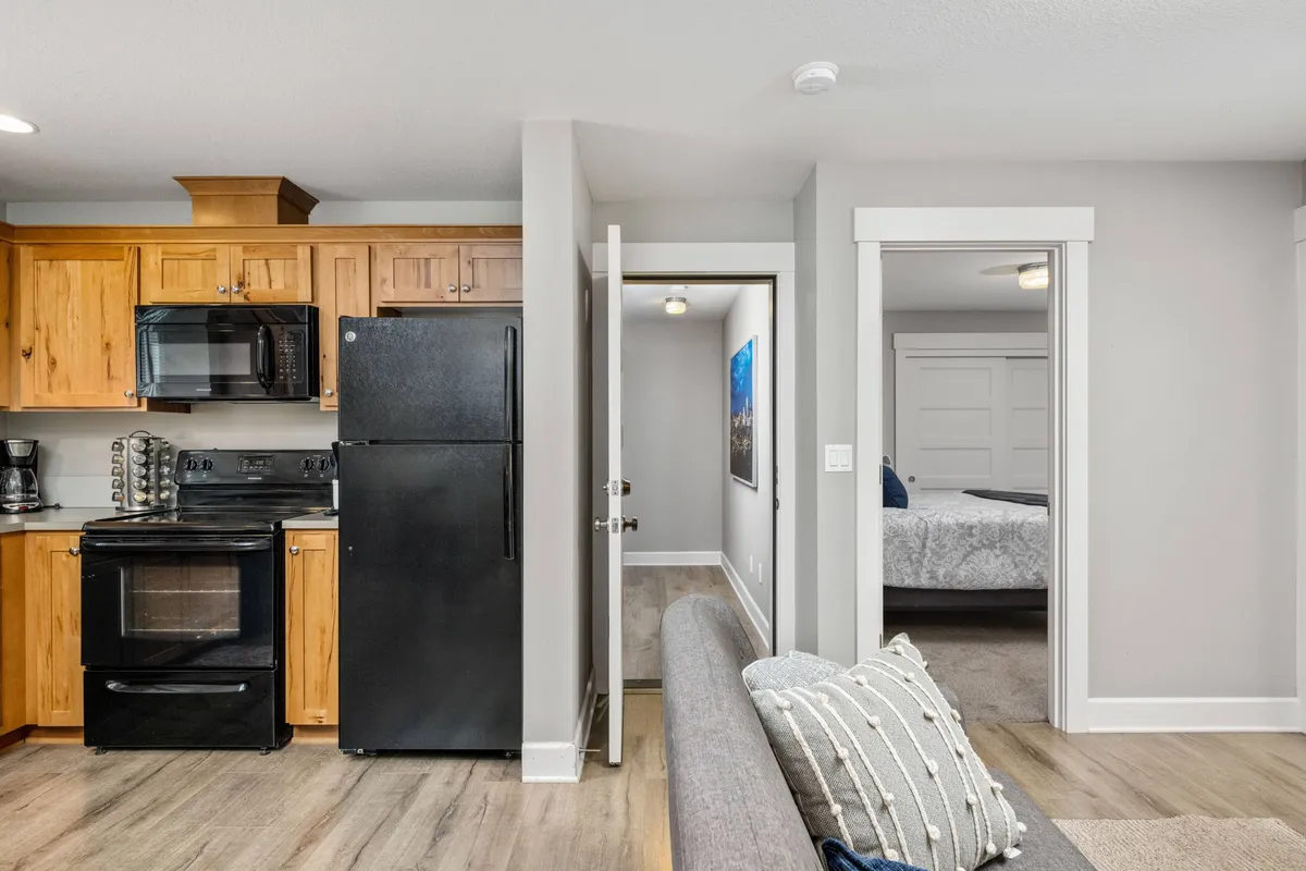 A warm, open-concept space showing the kitchen with modern appliances, a comfortable couch, and doorways leading further into the home. The view suggests a seamless transition between living and dining areas, evoking the sense of shared meals and togetherness before or after outdoor outings.