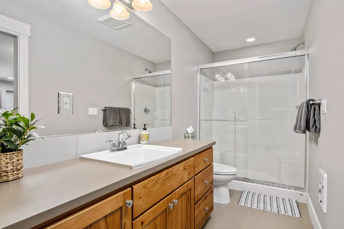 A sparkling clean bathroom with a modern sink and faucet, a wooden vanity, a stylish shower area, and a decorative plant. Natural light streams in, highlighting the inviting and fresh ambiance of the space.