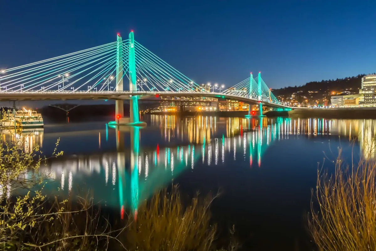A striking evening scene of a bridge spanning calm waters, with reflections of city lights shimmering on the surface. The mood is lively yet serene, capturing the excitement and romance of urban life, especially during twilight strolls by the river.